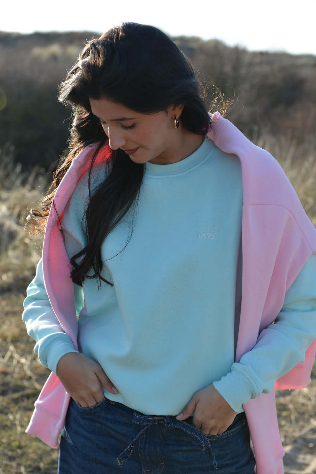 Model wearing mint Essential Crewneck sweater with relaxed fit, styled with a pink jacket outdoors.