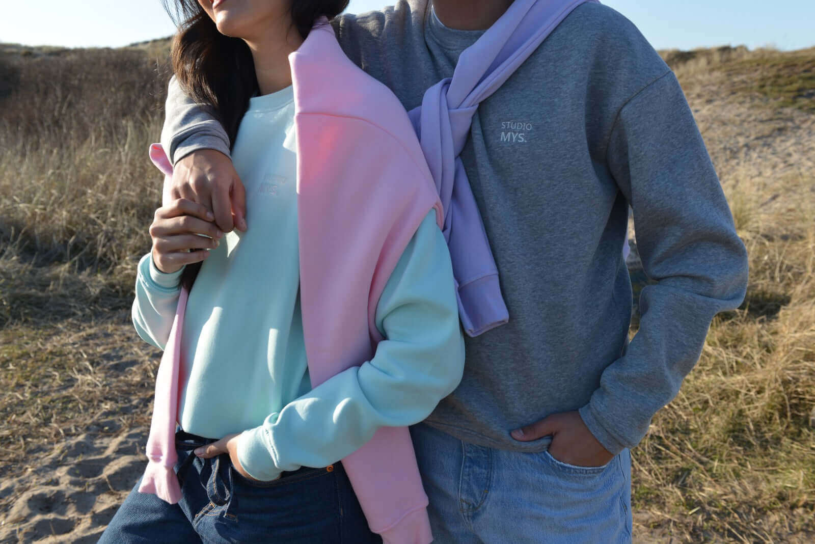 A stylish couple wearing cozy gray and pastel sweaters, embodying comfort and casual elegance in a natural setting.